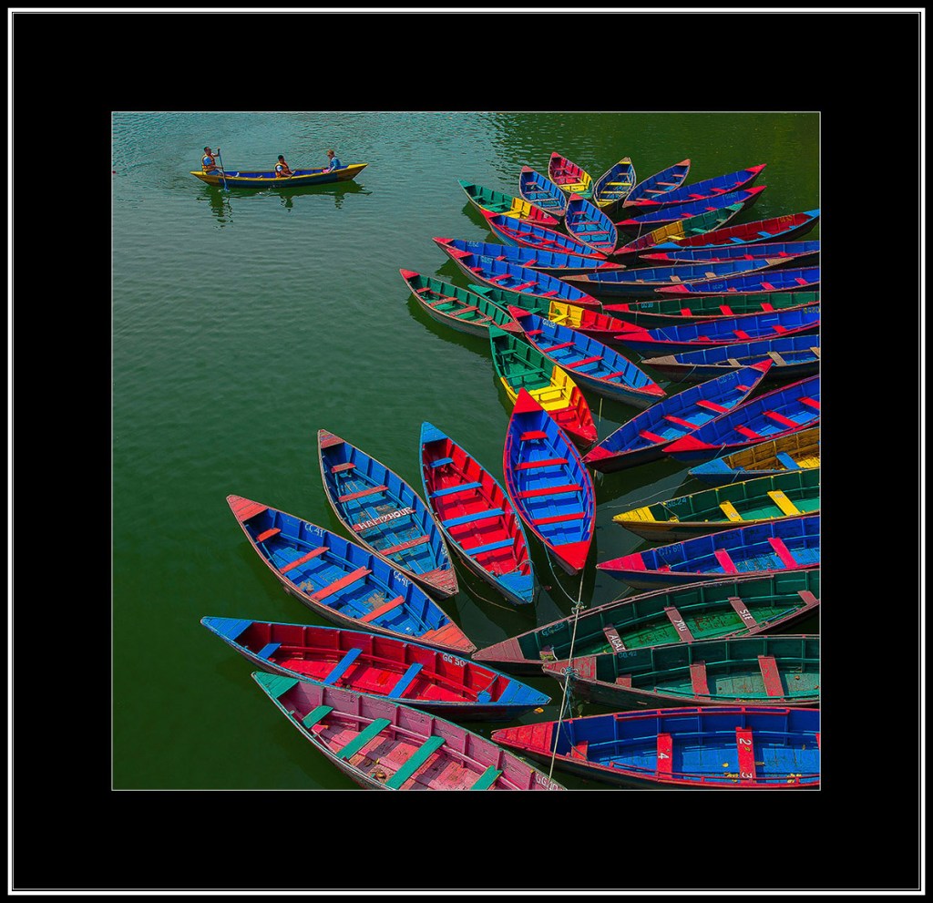 Aerial view of colorful traditional boats arranged in a floral pattern on green water.